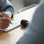 una persona entrevistando a otra con un cuaderno y una grabadora sobre la mesa